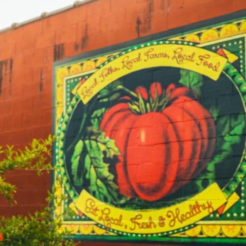 A beautiful community awaits a brick wall with a painting of a vegetable on it